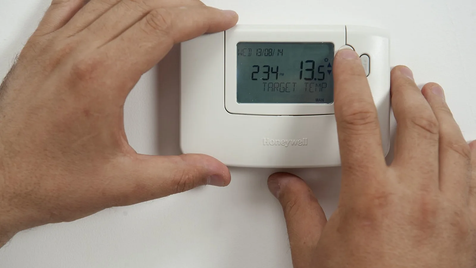 Mano ajustando un termostato de calefacción en la pared