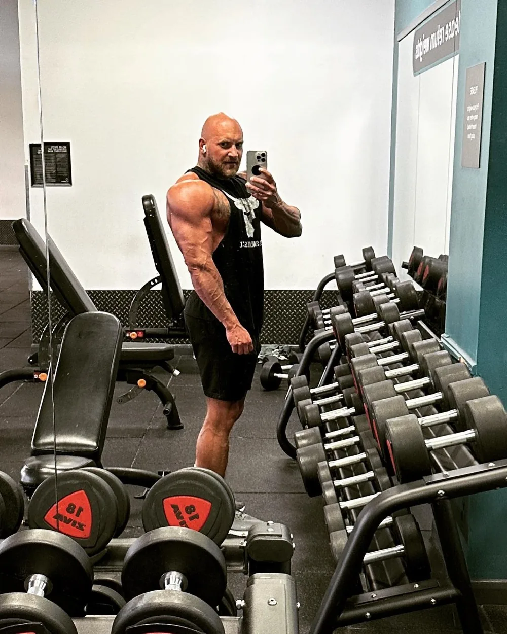 Mateusz Chmura se hace una foto en el espejo de un gimnasio junto a un estante de mancuernas