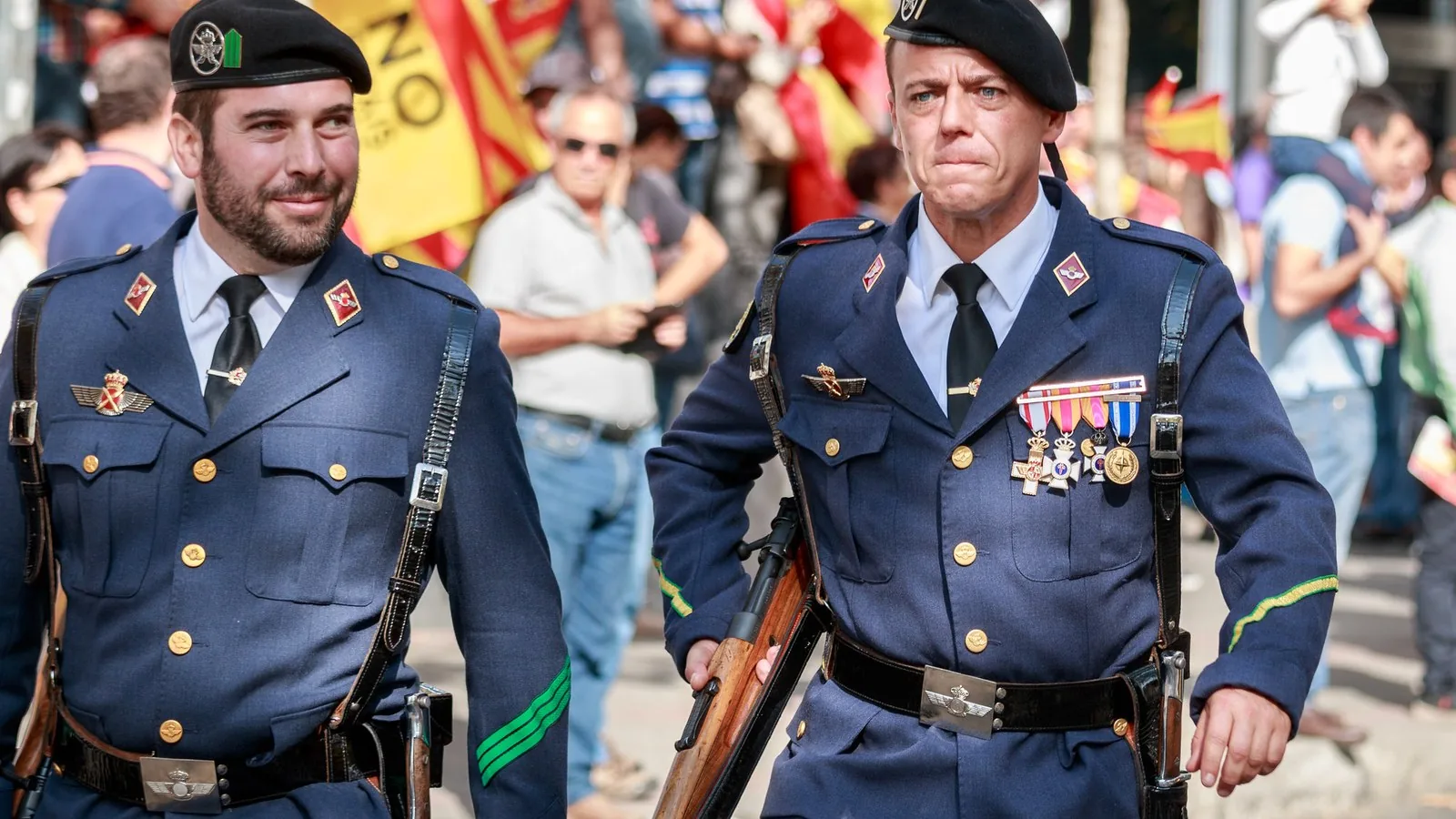 Dos militares del Ejército del Aire desfilan con banderas de España al fondo durante el desfile del 12 de octubre en Madrid