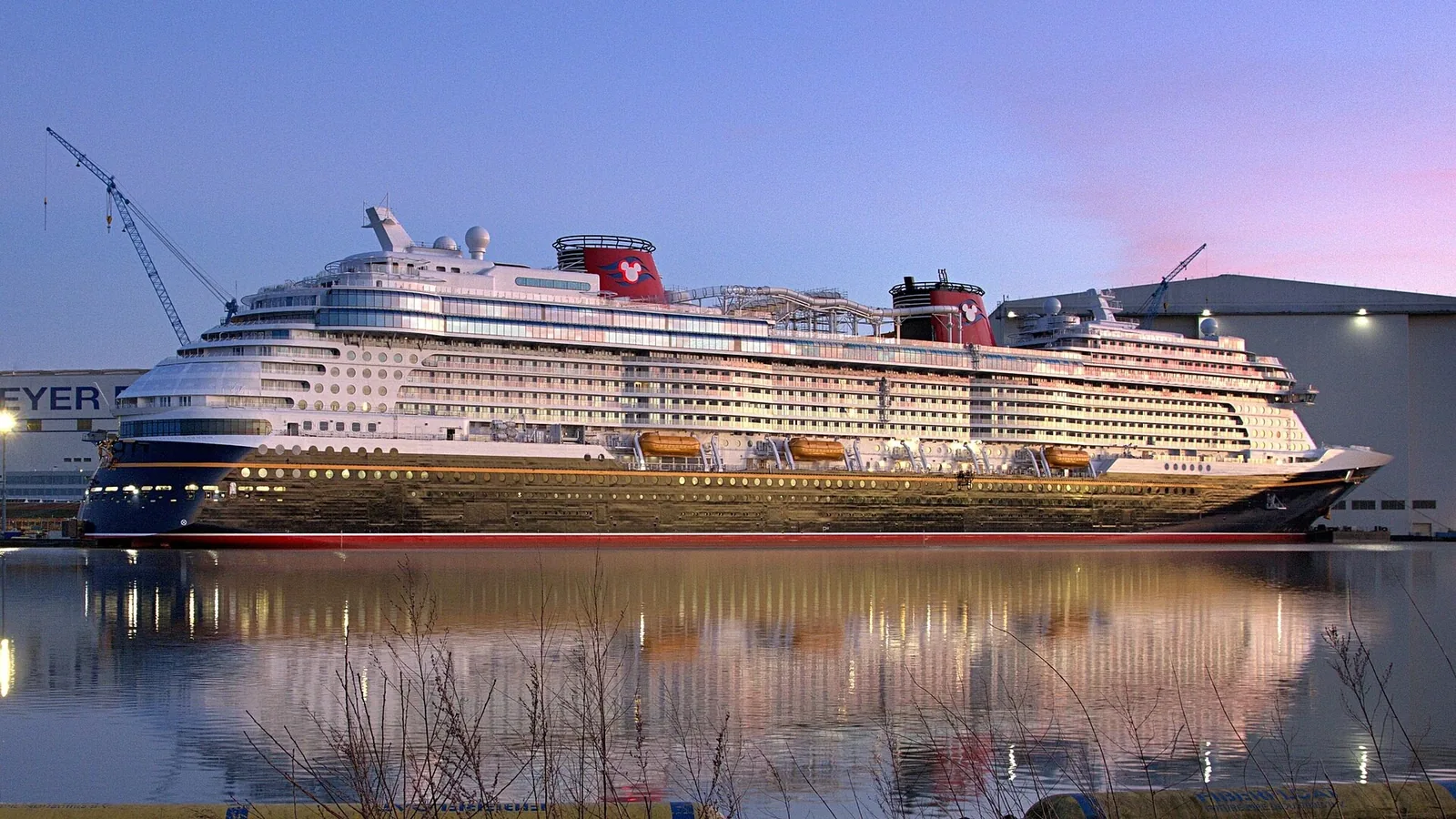 El crucero Disney Wish iluminado al atardecer en el astillero de Papenburg