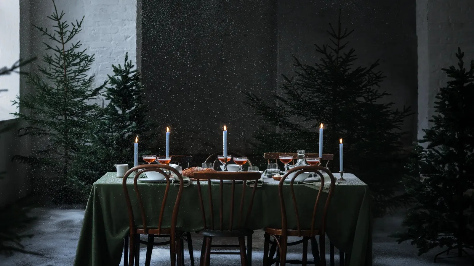 Mesa con mantel verde, velas encendidas y abetos en un comedor