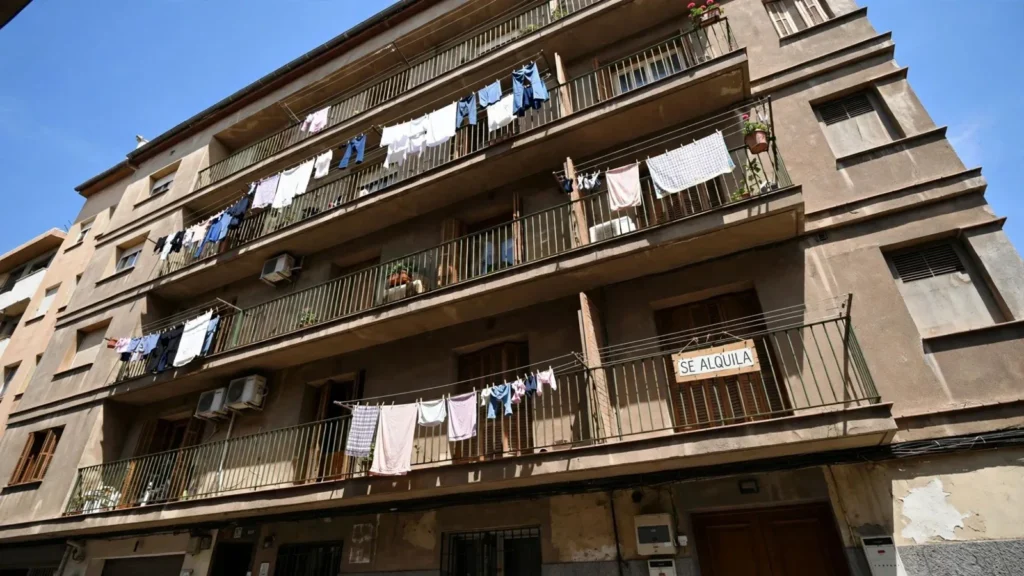 Fachada de un edificio de viviendas con ropa tendida y un cartel de se alquila en un balcón