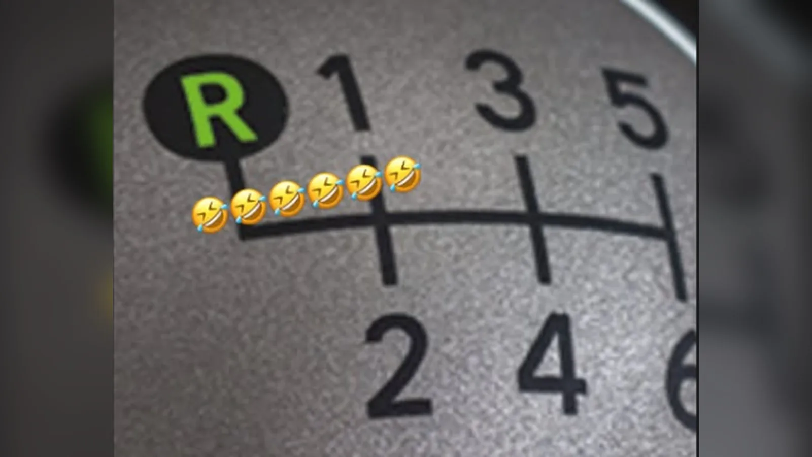 Palanca de cambios de coche con la marcha atrás, la R, iluminada en verde y varios emojis riendo